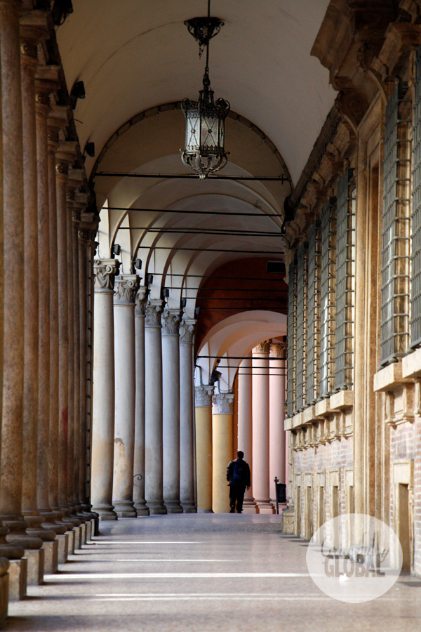 A man standing below a distant portico in Bologna looks up and away.